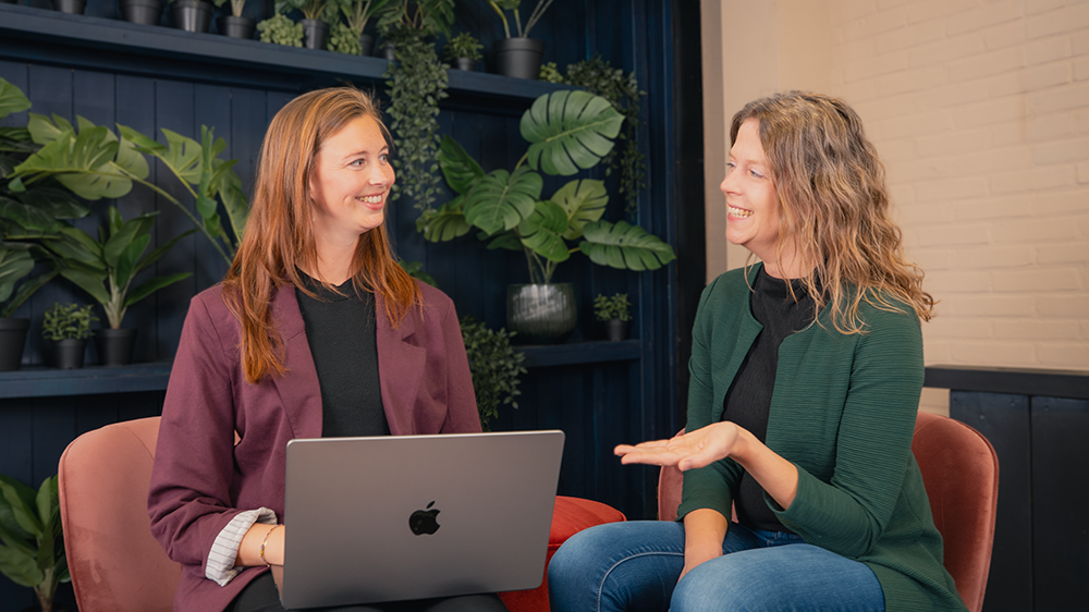 Foto van Marlena en Helen die aan het overleggen zijn. Marlena heeft een laptop op haar schoot en Helen gebaart.
