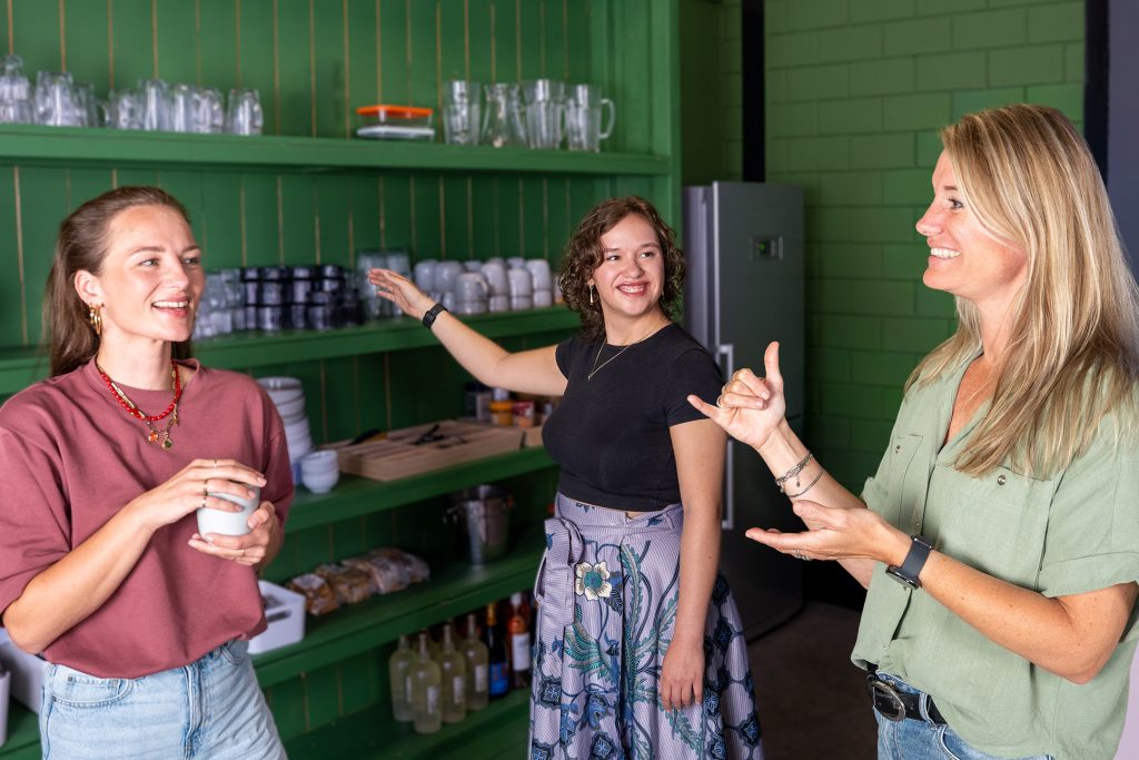 Teresa, Noemi en Muriel staan lachend met elkaar te praten in een groene keukenruimte.